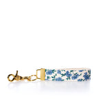 Introducing the Rustic Marlin Keychain - Blueberry by Rustic Marlin: This elegant keychain features gold hardware and a fabric strap adorned with a blue floral pattern on a white background, beautifully displayed on a white surface. Designed to double as a chic bag charm, its sturdy brass key clip keeps your keys secure and within easy reach. by Sea Bags