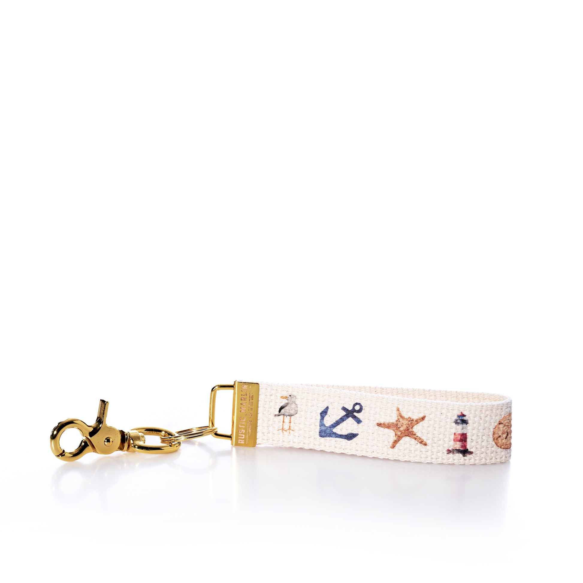 Introducing the Rustic Marlin Keychain - Summer Icons from Rustic Marlin. This keychain wrist strap showcases nautical-themed icons such as an anchor, starfish, lighthouse, and seashell printed on a white fabric band, complete with a gold clasp. The versatile design makes it perfect not just as a keyholder but also as a stylish bag charm or a unique souvenir for your collection. by Sea Bags
