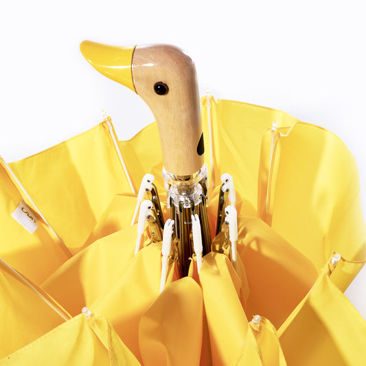 The Original Duck Head Umbrella - Yellow by ODH Limited t/a Original Duckhead features a delightful wooden handle shaped like a duck’s head, crafted from recycled umbrella materials and PFAS free yellow fabric panels, displayed against a clean white background. by Sea Bags