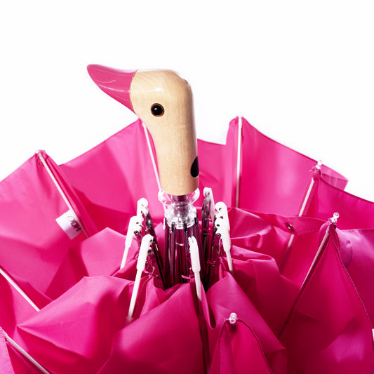 An upright Original Duck Head Umbrella - Pink by ODH Limited t/a Original Duckhead, with its signature duck head-shaped handle, is set against a white background. This durable umbrella blends playful design with practical reliability. by Sea Bags