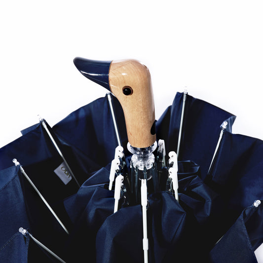 The Original Duck Head Umbrella - Navy by ODH Limited t/a Original Duckhead is displayed closed against a white background. Featuring a compact design, this umbrella showcases a handle shaped like a duck’s head with a wooden texture and a black beak, combining stylish charm with practical rain protection. by Sea Bags