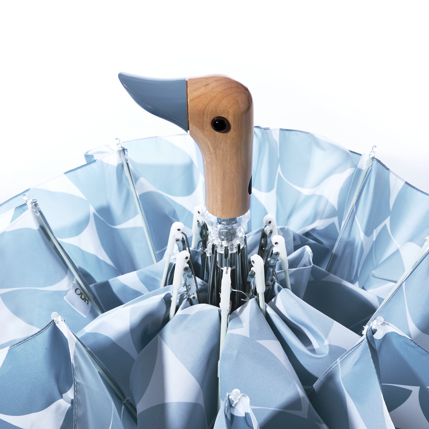 A partially open Original Duck Head Umbrella - Denim Moon Print by ODH Limited t/a Original Duckhead is shown from above, featuring a blue and white design and the brand’s signature duck-shaped handle. This charming, wind-resistant umbrella combines style and practicality for rainy days.