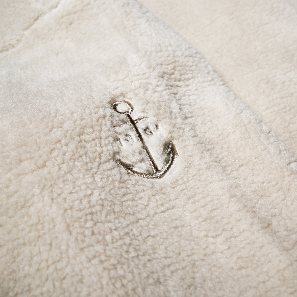 Close-up of the Fleece Button-Front Coat - Moonstruck by Batela USA Inc, featuring soft cream fleece with an embroidered anchor—ideal for coastal adventures.