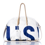 The Vintage US 52 Weekender by Sea Bags, featuring white and navy blue hues, rope handles, a white shoulder strap, and a Sea Bags tag attached, is displayed on a reflective surface. by Sea Bags
