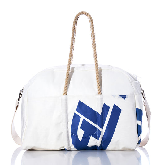The Sea Bags Vintage Ideal 18 Weekender, featuring blue graphic print, hemp handles, side shoulder strap, and external pockets, is displayed on a reflective surface. by Sea Bags