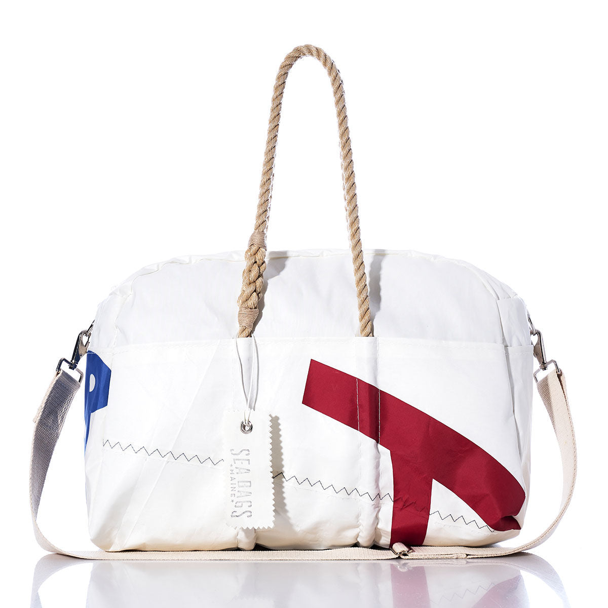 The Sea Bags Vintage Harbor 20 Weekender features a white exterior with tan rope handles, a cream shoulder strap, and striking red and blue graphic accents—making it the perfect choice for a vintage-inspired harbor getaway or as a stylish weekender bag. An attached tag reading seabags.lifepletes the look. by Sea Bags