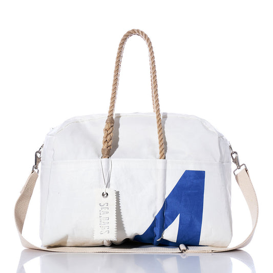 Introducing the Sea Bags Vintage Blue 4 Weekender: a white duffle bag with sturdy rope handles, a removable beige shoulder strap, and an eye-catching blue geometric design on the front. Ideal for weekend getaways, this versatile bag features a white “SEABAGS” tag attached to one handle. by Sea Bags