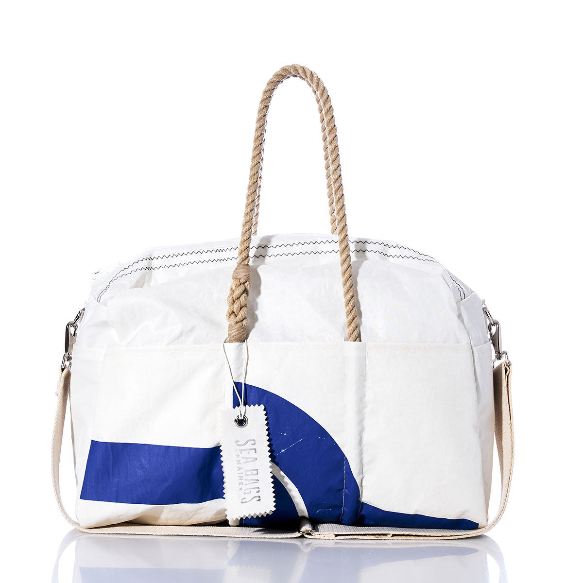 Sea Bags Vintage JY Weekender—a white and blue duffel bag featuring rope handles, a beige shoulder strap, and a white SEABAGS tag—displayed on a reflective surface against a white background; the ideal choice for your vintage-inspired getaway or stylish weekend travel. by Sea Bags