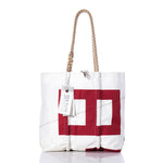 Introducing the Sea Bags Vintage 843 Medium Tote, a white bag adorned with a bold red geometric print. Crafted in Maine, it features hand-spliced rope handles, distinctive zigzag stitching, and an attached tag displaying the Sea Bags name. This vintage sail tote from our Maine crafted bags collection is showcased against a clean white background. by Sea Bags
