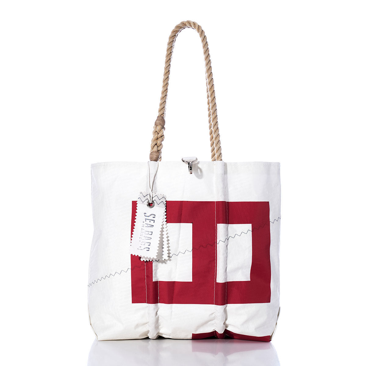 Introducing the Sea Bags Vintage 843 Medium Tote, a white bag adorned with a bold red geometric print. Crafted in Maine, it features hand-spliced rope handles, distinctive zigzag stitching, and an attached tag displaying the Sea Bags name. This vintage sail tote from our Maine crafted bags collection is showcased against a clean white background. by Sea Bags
