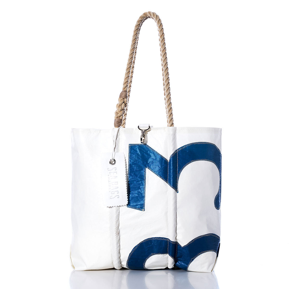 Introducing the Sea Bags Vintage 1083 Medium Tote: expertly handcrafted in Maine from recycled white sailcloth, it features sturdy hand-spliced rope handles and a bold navy-blue letter M applique. A branded Sea Bags paper tag attached to the handle highlights its unique, original origin. by Sea Bags