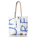 Sea Bags’ Vintage Blue Letters Medium Tote features a white canvas body adorned with original sail insignia and blue abstract lettering, reminiscent of classic designs. The tote is finished with hand-spliced rope handles, signature zigzag stitching, and a white SEABAGS tag attached to one handle. by Sea Bags
