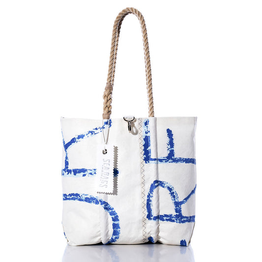 Sea Bags’ Vintage Blue Letters Medium Tote features a white canvas body adorned with original sail insignia and blue abstract lettering, reminiscent of classic designs. The tote is finished with hand-spliced rope handles, signature zigzag stitching, and a white SEABAGS tag attached to one handle. by Sea Bags