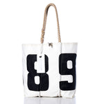 The Sea Bags Vintage 89 Medium Tote features bold black 89 numbers on a white background, hand-spliced rope handles, and an attached white tag. Photographed on a white backdrop, this classic Maine handcrafted bag is inspired by the iconic vintage sail tote. by Sea Bags