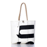 The Sea Bags Vintage US-8 Medium Tote features a white canvas body with a bold black letter graphic, hand-spliced rope handles, and an attached white tag. Inspired by classic Maine sail totes and photographed on a clean white background, this bag embodies the enduring charm and craftsmanship of Maine-made accessories. by Sea Bags