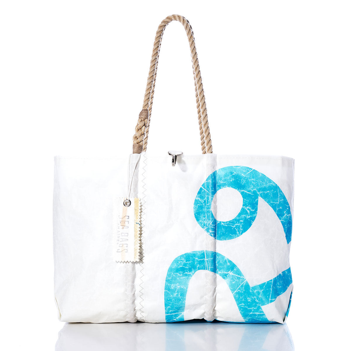 Introducing the Sea Bags Vintage Rhodes 19 Large Tote—a handmade Maine bag crafted from white sailcloth with a striking blue abstract design, sturdy rope handles, and a rectangular tag attached. Photographed against a white background, this tote artfully combines classic style with nautical charm. by Sea Bags