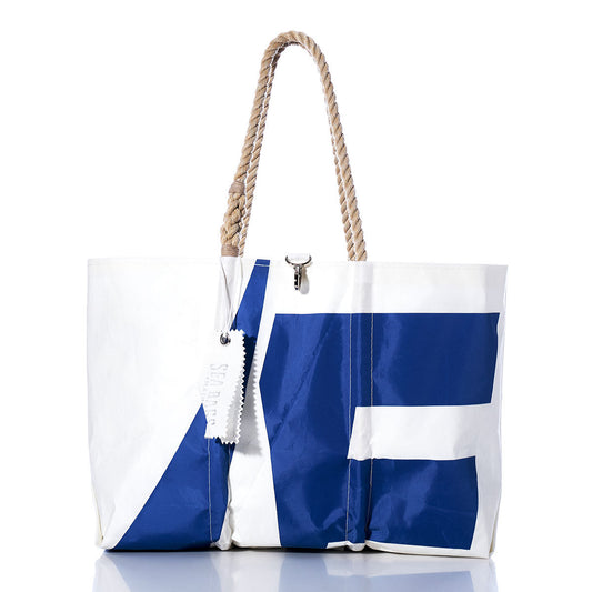 The Sea Bags Vintage Etchells Large Tote is a spacious white sailcloth bag adorned with a striking blue geometric pattern. It features sturdy rope handles and a discreet white tag, all showcased against a crisp white background with a subtle reflection. Handmade in Maine, this tote embodies classic nautical style. by Sea Bags