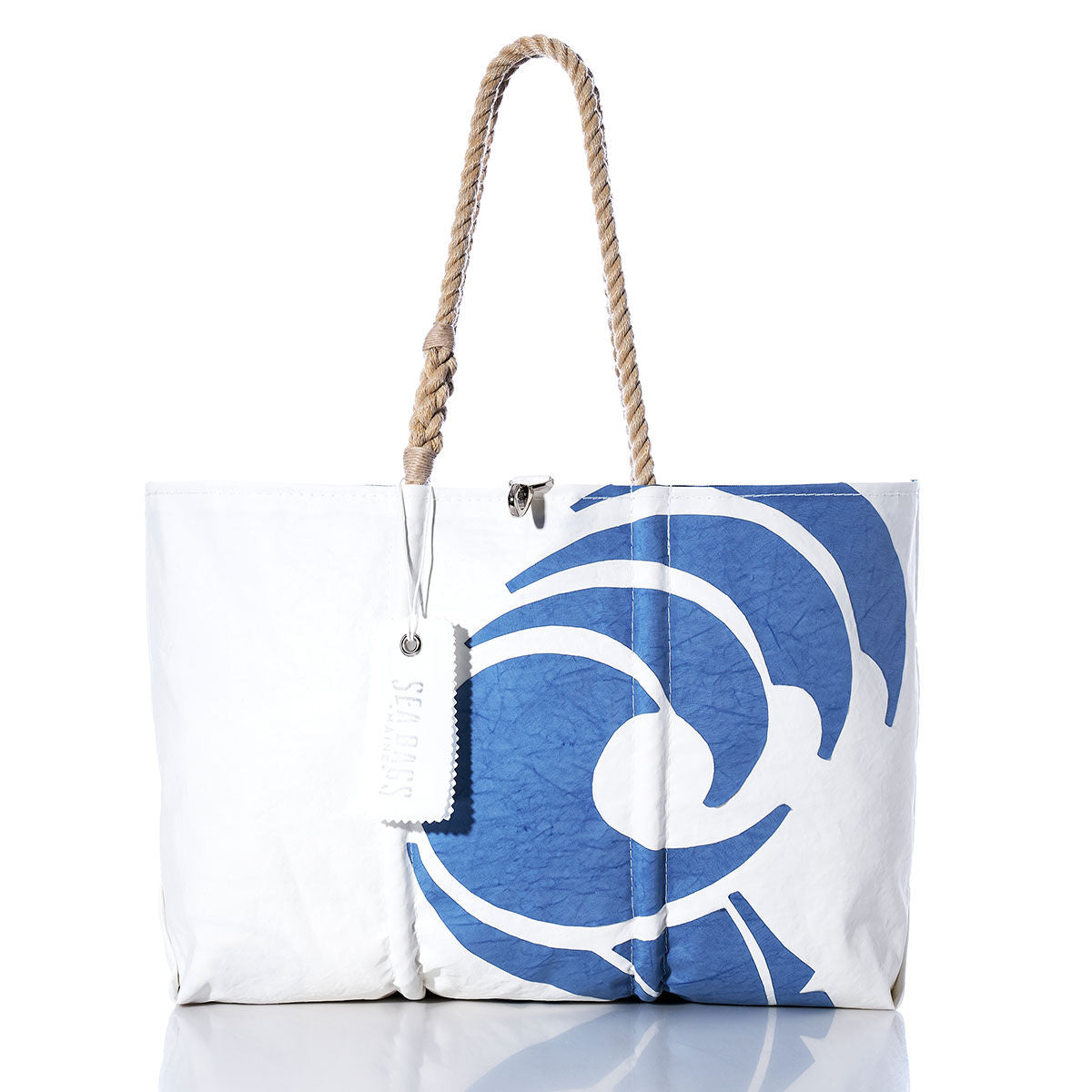 Sea Bags’ Vintage Beneteau Large Tote is a white sailcloth tote bag featuring a blue abstract swirl design, sturdy rope handles, and a white tag, elegantly displayed against a white background. This handcrafted piece captures the timeless style unique to the Sea Bags brand. by Sea Bags