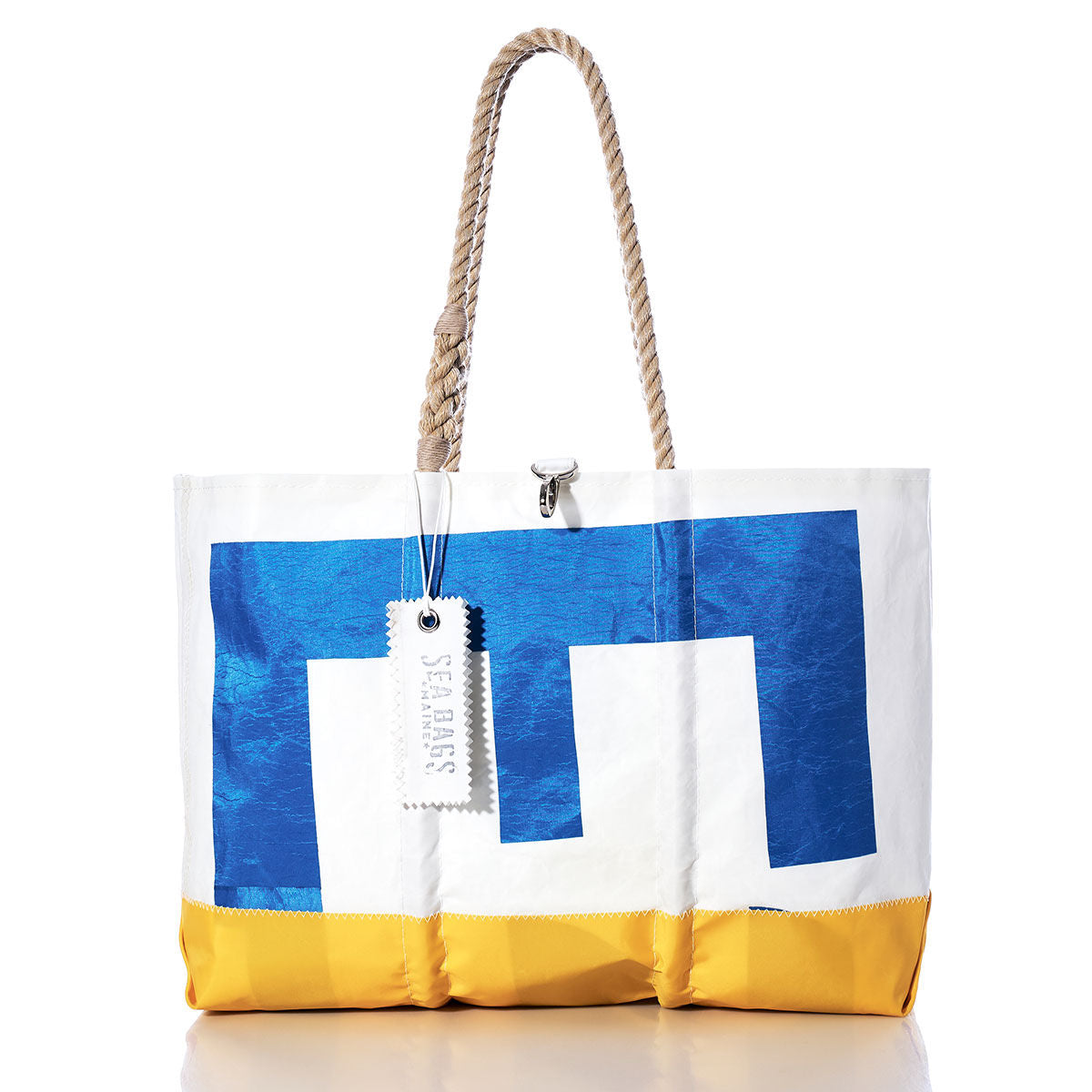 Vintage Etchells 22 Ogunquit Beach Tote by Sea Bags crafted from recycled sail cloth, showcases a blue and white geometric pattern with a yellow base, sturdy rope handles, and a signature white Sea Bags tag—photographed against a white background. This tote blends the nostalgic appeal of vintage sail bags with lasting durability and nautical flair. by Sea Bags