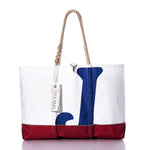 The Vintage J24 Ogunquit Beach Tote by Sea Bags features a striking white and red design with a blue anchor motif, rope handles, and a white tag near the top. Crafted from recycled sail cloth, this tote seamlessly blends style and sustainability for all your seaside adventures. by Sea Bags