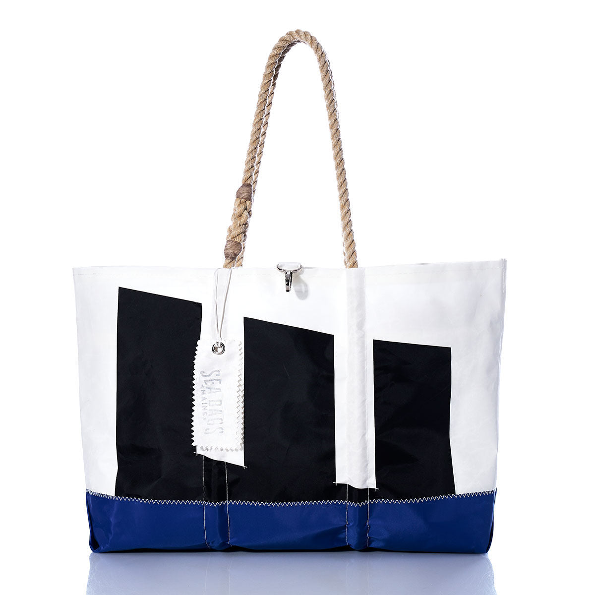 The Sea Bags Vintage Etchells Ogunquit Beach Tote is a large white beach bag crafted from recycled sail cloth, featuring bold black geometric shapes, a blue bottom edge, sturdy rope handles, and a white tag attached—all inspired by vintage Etchells sails. by Sea Bags