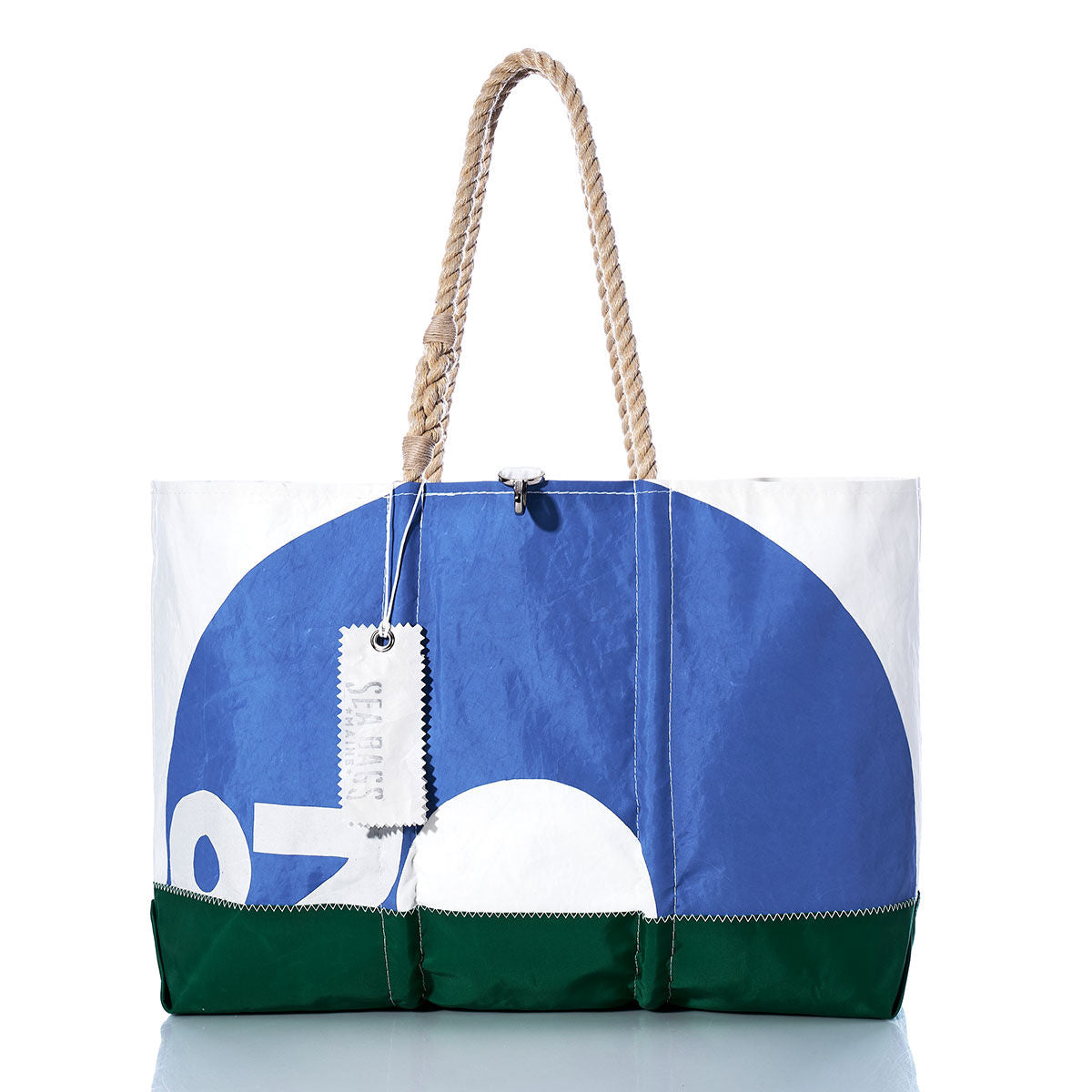 The Sea Bags Vintage O-Day Ogunquit Beach Tote features bold blue, white, and green color blocks, sturdy rope handles, and a tag attached. Crafted from recycled sail cloth, this spacious tote is photographed on a reflective surface with a white background. by Sea Bags