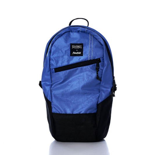 Introducing the Sea Bags Vintage Blue Crew Backpack, crafted from recycled sail cloth and designed with a striking blue and black color combination. It features a front zipper pocket and is accented with a SEA BAGS logo label on the upper front. Displayed against a white background, this sustainable backpack from Sea Bags seamlessly blends eco-conscious craftsmanship with timeless style. by Sea Bags