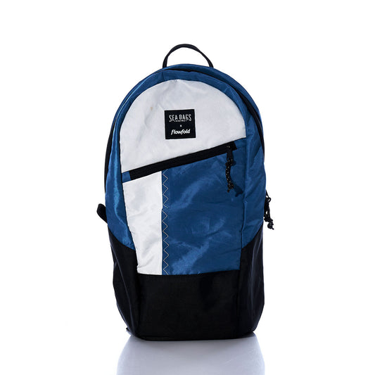 The Sea Bags Vintage Blue and White Crew Backpack, crafted from recycled sail cloth, stands upright against a white background. This sustainable backpack features a front zipper pocket, a SEA BAGS patch logo, and blends eco-conscious design with stylish appeal. by Sea Bags