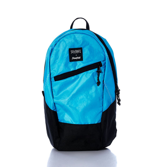 Sea Bags Vintage Blue Crew Backpack in blue and black, featuring a front zip pocket, black bottom panel, and a Flowfold label. Crafted from recycled sail cloth for a sustainable choice, this backpack is shown against a white background. by Sea Bags