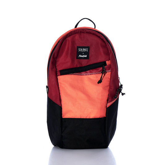 Sea Bags Vintage Red and Orange Crew Backpack, crafted from recycled sail cloth with bold red, orange, and black color blocks, features a front zipper pocket, black bottom, and a small top handle. Shown against a white background. by Sea Bags
