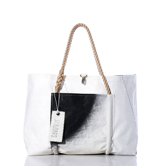 Introducing the Sea Bags Vintage Black and White Wharf Tote—a handcrafted bag made in Portland, Maine from recycled sails. This durable tote features a striking large black patch on white, visible stitching, sturdy rope handles, a hanging tag labeled SEA BAGS, and a top-center clasp for secure closure. It combines nautical charm with sustainability in every detail. by Sea Bags