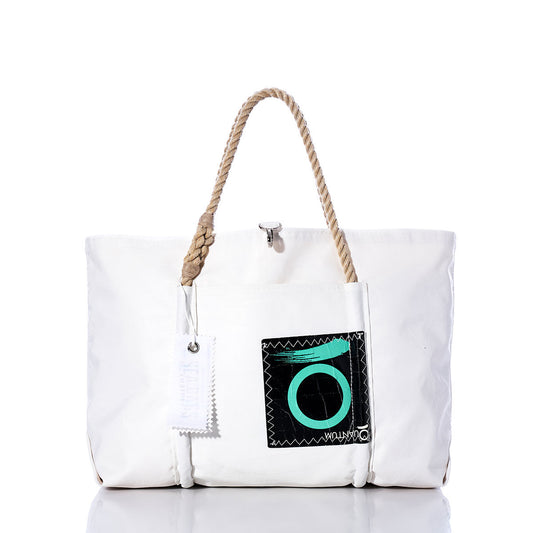 Sea Bags Vintage Quantum Wharf Tote is a handcrafted white canvas bag featuring tan rope handles and a black front pocket adorned with a teal circular design. Inspired by the coastal charm of Portland, Maine, this recycled sail tote includes a white tag hanging from one handle and is shown against a white background. by Sea Bags
