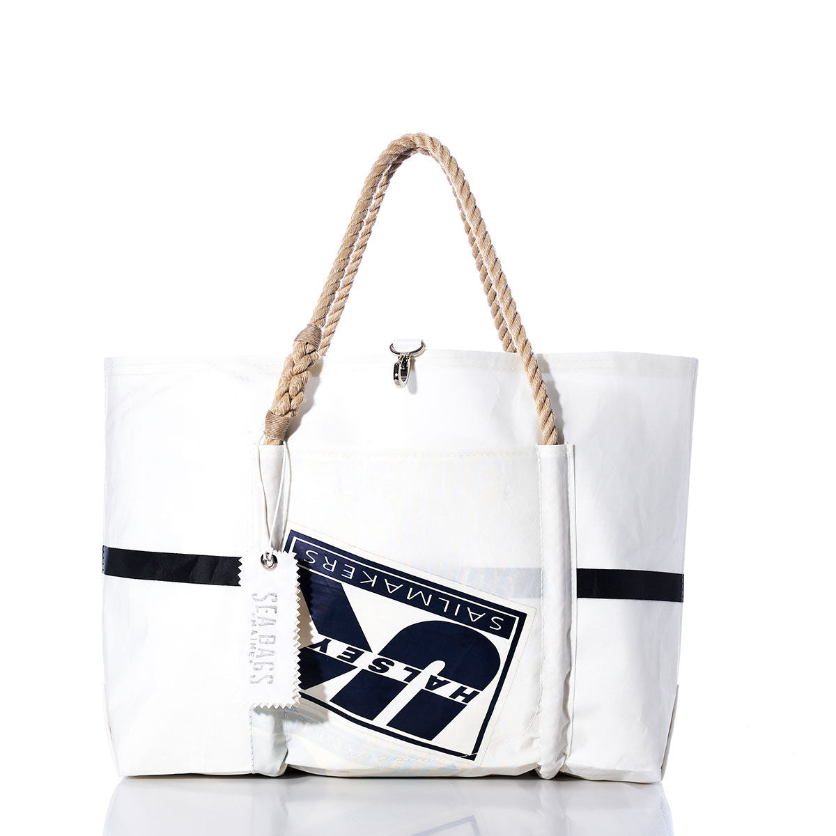 The Sea Bags Vintage UK Sailmakers Wharf Tote is a white handcrafted tote bag, made from recycled sails, featuring a rope handle, a navy logo patch, and a white SEABAGS tag. Displayed against a white background, this tote is inspired by the classic design of the Vintage UK Sailmakers Wharf Tote. by Sea Bags