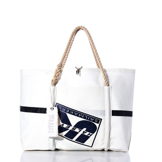 The Sea Bags Vintage UK Sailmakers Wharf Tote is a white handcrafted tote bag, made from recycled sails, featuring a rope handle, a navy logo patch, and a white SEABAGS tag. Displayed against a white background, this tote is inspired by the classic design of the Vintage UK Sailmakers Wharf Tote. by Sea Bags