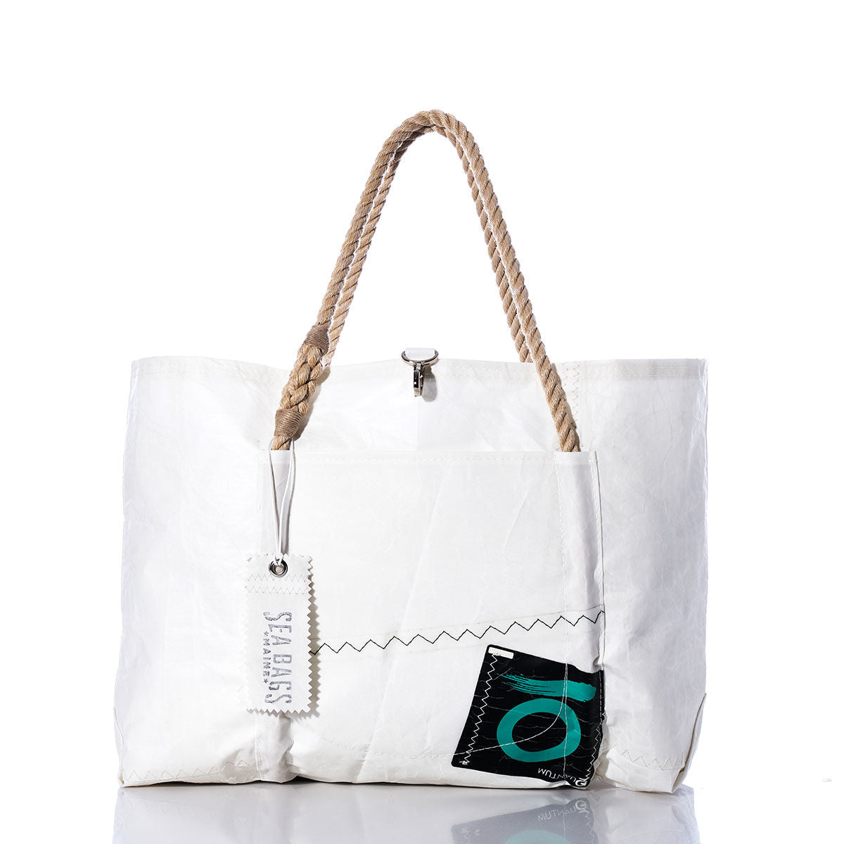 Introducing the Sea Bags Vintage Quantum Wharf Tote—a white, handmade tote bag crafted in Portland, Maine from recycled sail material. This eco-friendly design features rope handles, a convenient front pocket, the signature SEA BAGS tag, and a distinctive black and green patch near the bottom right corner. The Vintage Quantum Wharf Tote combines practical style with sustainable craftsmanship. by Sea Bags