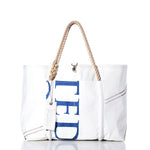 The Sea Bags Vintage TED Wharf Tote is a white recycled sail bag with rope handles, blue lettering on the side, a front pocket, and visible stitching details—showcased against a white background. Inspired by the iconic wharf tote and handmade in Portland, Maine. by Sea Bags