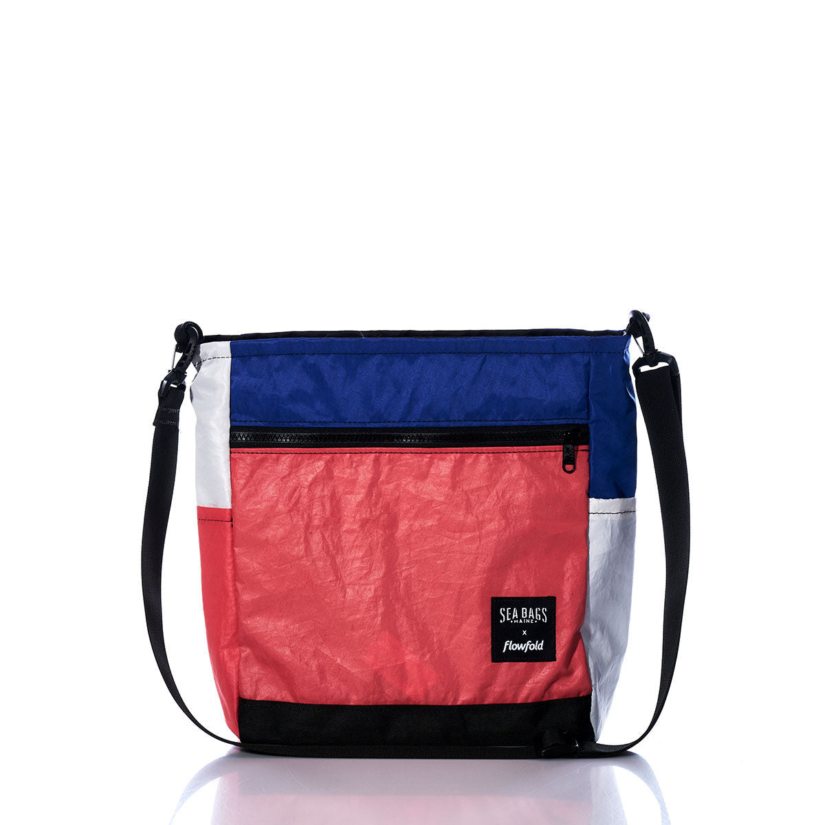 Introducing the Vintage Blue and Orange Medium Voyager Crew Crossbody by Sea Bags. This sustainable crossbody bag features bold blue, orange, white, and black color-blocked panels crafted from recycled sail cloth. Designed with a convenient front zip pocket, black strap, and finished with a “Sea Bags” patch on the front, this eco-conscious accessory combines striking style with responsible materials. by Sea Bags