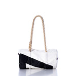 The Sea Bags Vintage Black 7 Baguette Bag is a white and black cylindrical bag featuring a thick, hand-spliced hemp rope handle. Displayed on a reflective surface against a white background, its classic vintage baguette shape is complemented by subtle sail insignias for a nautical touch. by Sea Bags
