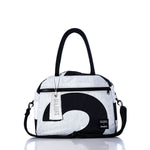 The Sea Bags Vintage Black 2 Essential Weekender Travel Bag is a white and black duffel featuring black handles, a front zipper pocket, and a removable shoulder strap. Perfect as a Weekender Travel Bag, it includes a white SEABAGS tag hanging from the handle and is reflected on the surface. by Sea Bags