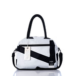 The Vintage Black and White Essential Weekender Travel Bag by Sea Bags features black handles, a front zipper pocket, an attached shoulder strap, and a branded tag reading Sea Bags. This versatile carry-on is displayed on a reflective white surface. by Sea Bags