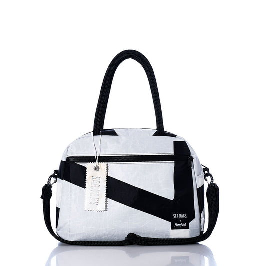 The Vintage Black and White Essential Weekender Travel Bag by Sea Bags features black handles, a front zipper pocket, an attached shoulder strap, and a branded tag reading Sea Bags. This versatile carry-on is displayed on a reflective white surface. by Sea Bags