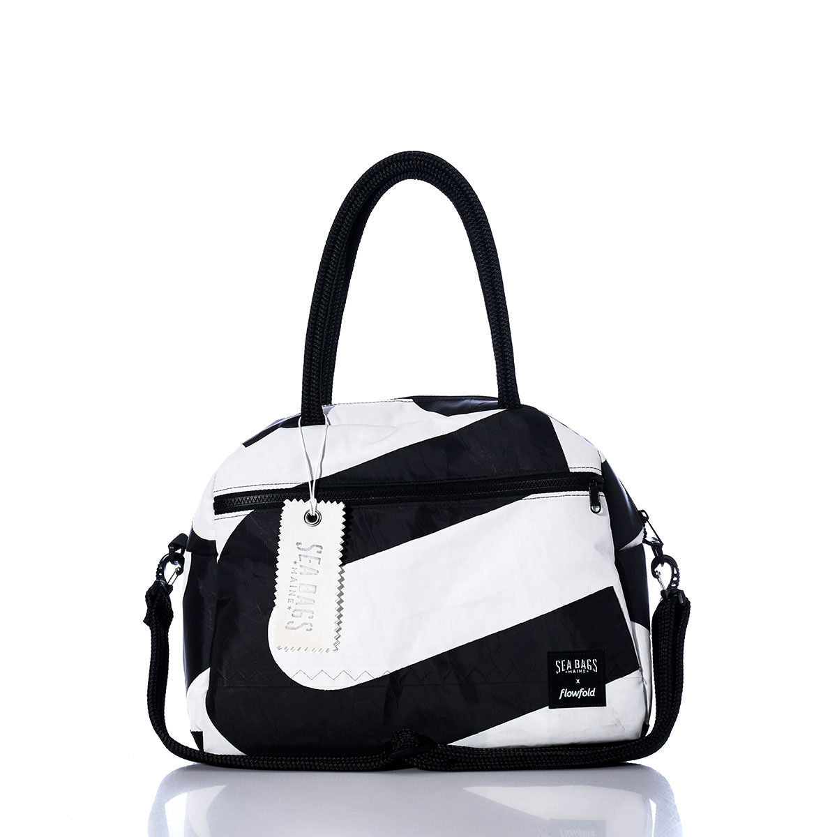 Sea Bags Vintage Black and White Essential Weekender Travel Bag features bold diagonal stripes in black and white, two sturdy handles, a front zippered pocket, a detachable shoulder strap, and a signature white tag. Designed to elevate your travel style, this chic carryon or weekender bag stands elegantly on a reflective surface. by Sea Bags