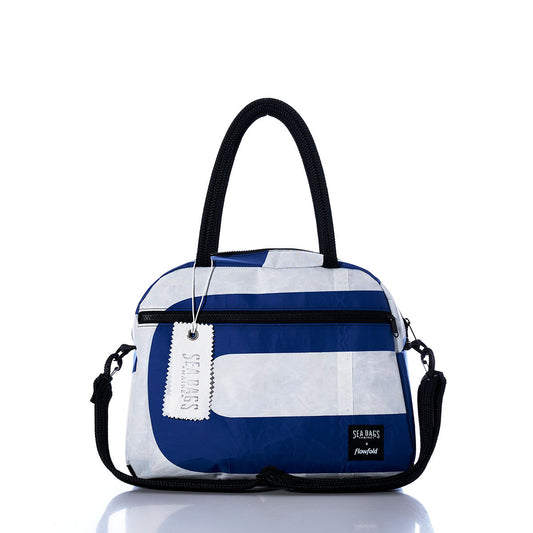 The Vintage US Essential Weekender Travel Bag by Sea Bags features a blue and white design with black handles and a zippered pocket, highlighted by the signature Sea Bags tag and logo on a reflective surface against a white background. Crafted as a compact carryon, this stylish bag is the perfect companion for your next getaway. by Sea Bags