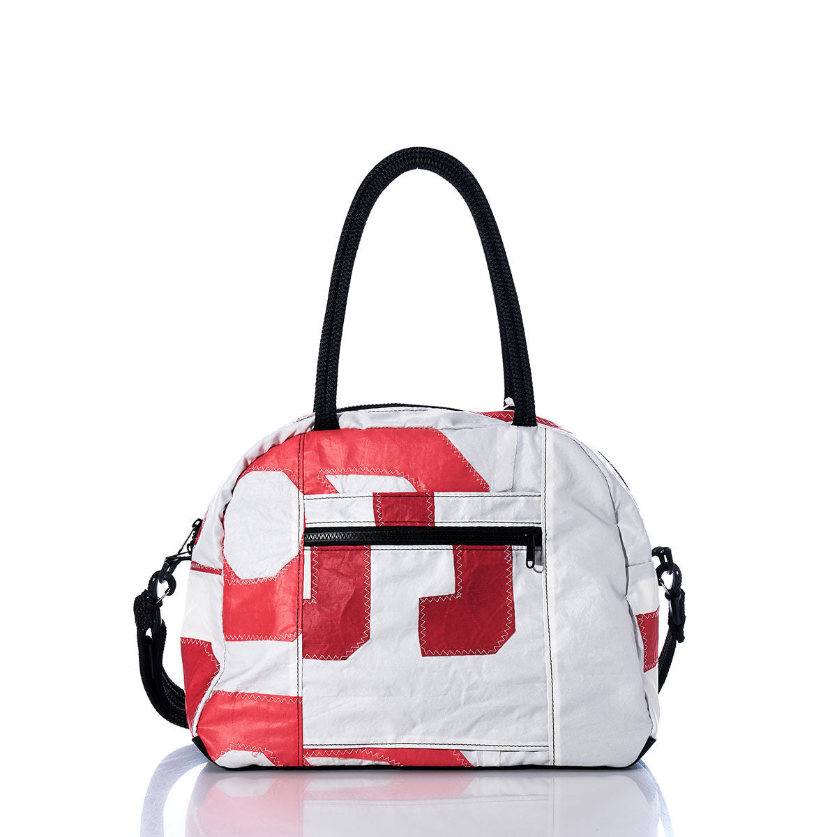 The Sea Bags Vintage Red Letters Essential Weekender Travel Bag features striking red geometric patterns reminiscent of vintage lettering on a white background, complemented by sturdy black handles, a front zippered pocket, and a detachable black shoulder strap. Shown here on a white reflective surface, it’s the ideal choice for an overnight stay or as a stylish weekender bag for your next getaway. by Sea Bags