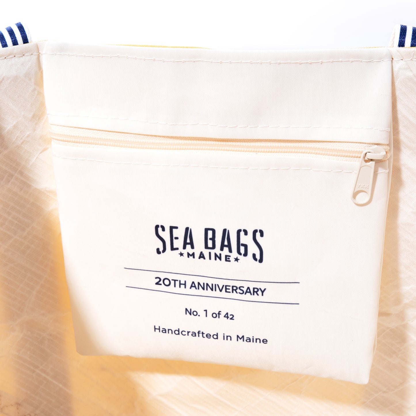 Close-up of a zippered pocket on a white Sea Bags Vintage Yellow Canvas Large Tote, labeled “SEA BAGS MAINE 20th Anniversary, No. 1 of 42, Handcrafted in Maine.” This limited edition tote is part of the Heritage Collection Tote series. by Sea Bags