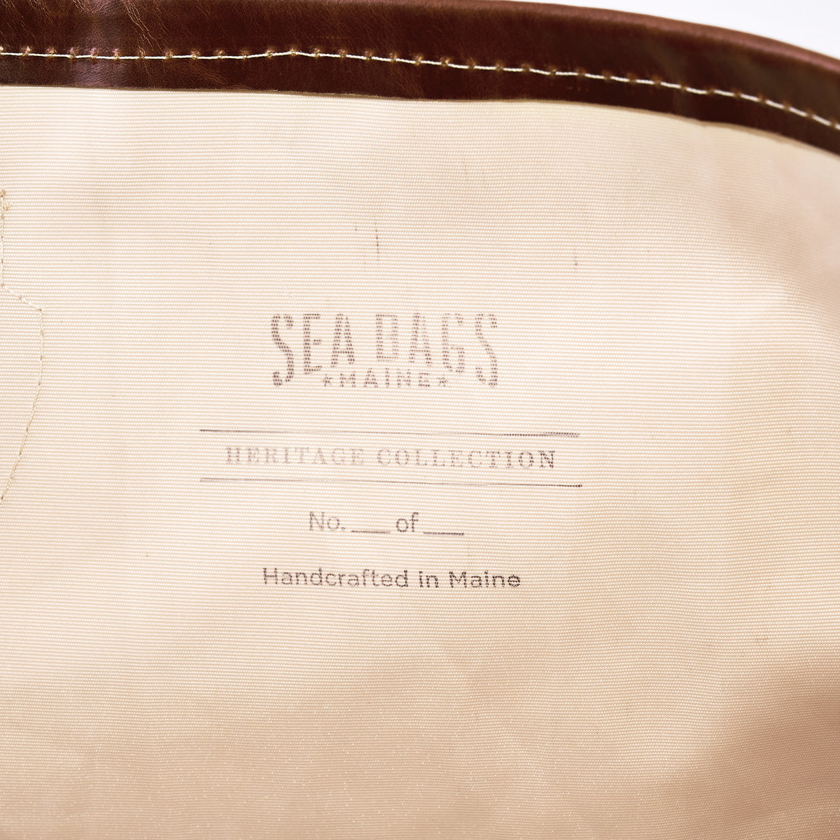 Certainly Here’s the revised sentence using your product data: A beige fabric label reads “SEA BAGS MAINE, HERITAGE COLLECTION, No. ___ of ___, Handcrafted in Maine,” with brown trim visible at the top—a subtle homage to classic yacht restoration traditions embodied by vessels like S/Y AELLO, which inspires the Sea Bags Heritage Aello Large Tote.