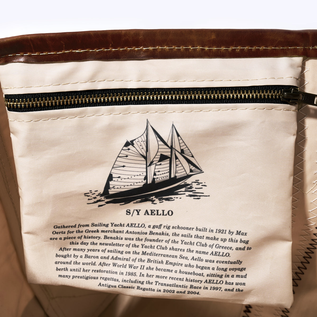 Close-up of a white fabric zippered pouch or bag with printed text and a sailboat illustration. The text references S/Y Aello and includes historical sailing details.