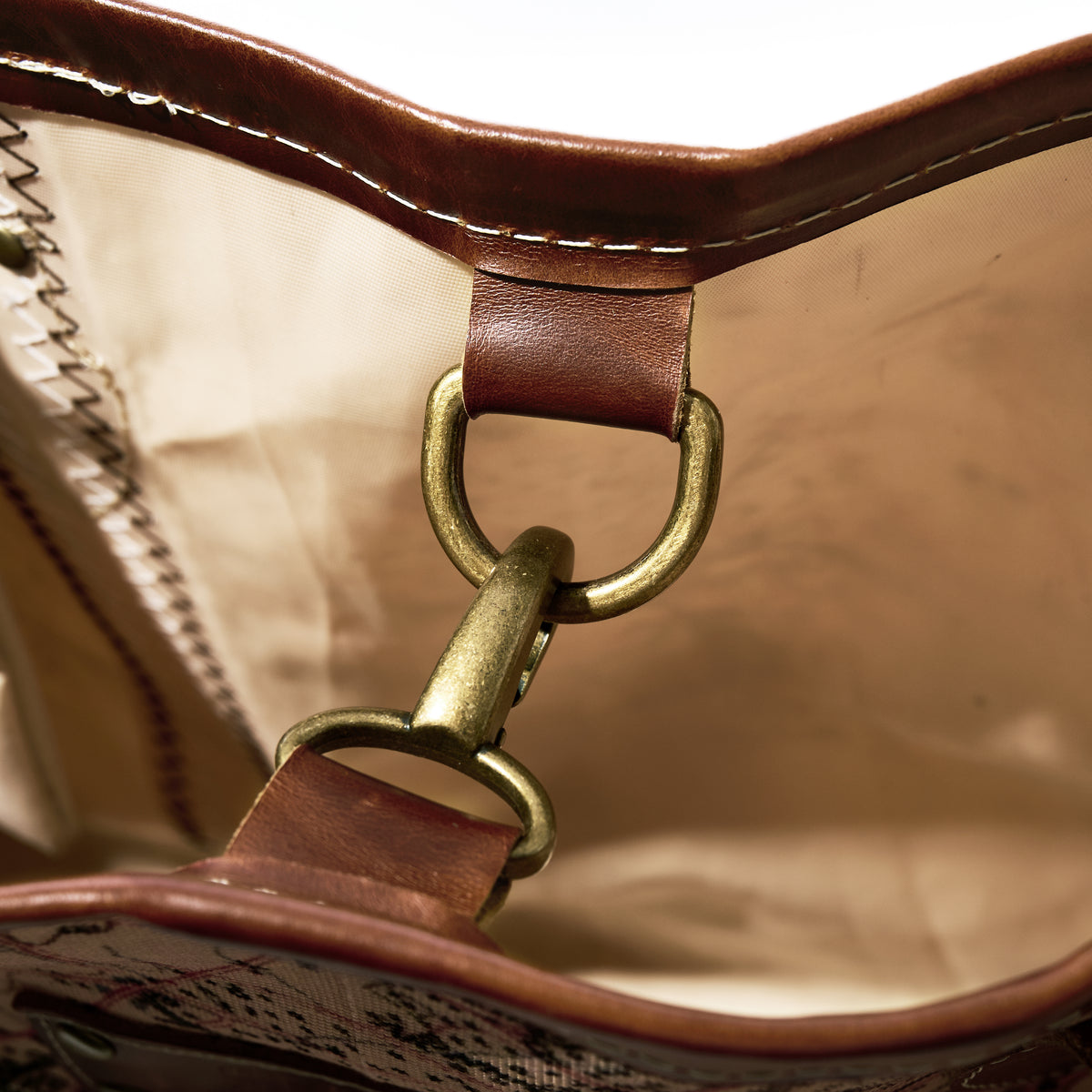 Close-up of the interior of the Heritage Aello Large Tote by Sea Bags, featuring a brass clasp joining two brown leather loops against a beige fabric lining—an example of meticulous craftsmanship inspired by the detailing found in classic yacht restorations like the famed Greek sailing yacht S/Y AELLO.
