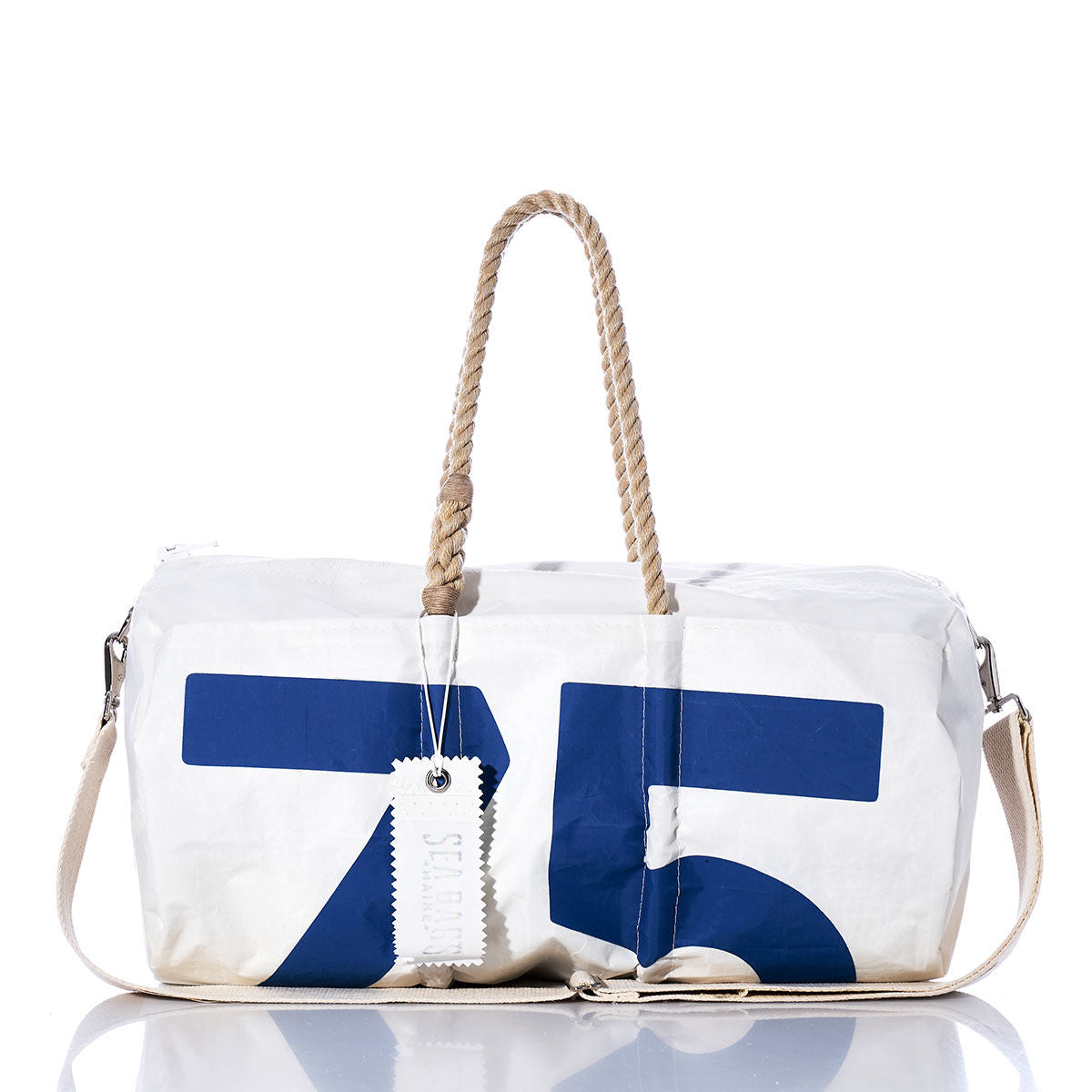 The Sea Bags Vintage Blue 75 Duffel, crafted from recycled sail cloth, showcases blue sail insignias with the number 75, beige rope handles, a beige shoulder strap, and a white tag. It is photographed against a white background. by Sea Bags