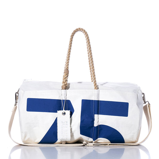 The Sea Bags Vintage Blue 75 Duffel, crafted from recycled sail cloth, showcases blue sail insignias with the number 75, beige rope handles, a beige shoulder strap, and a white tag. It is photographed against a white background. by Sea Bags